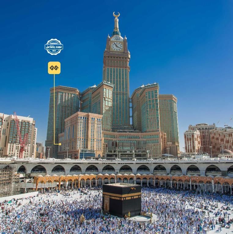 The Kaaba at the center of a crowded mosque, overlooked by the clock tower of the Abraj Al-Bait, Mecca.