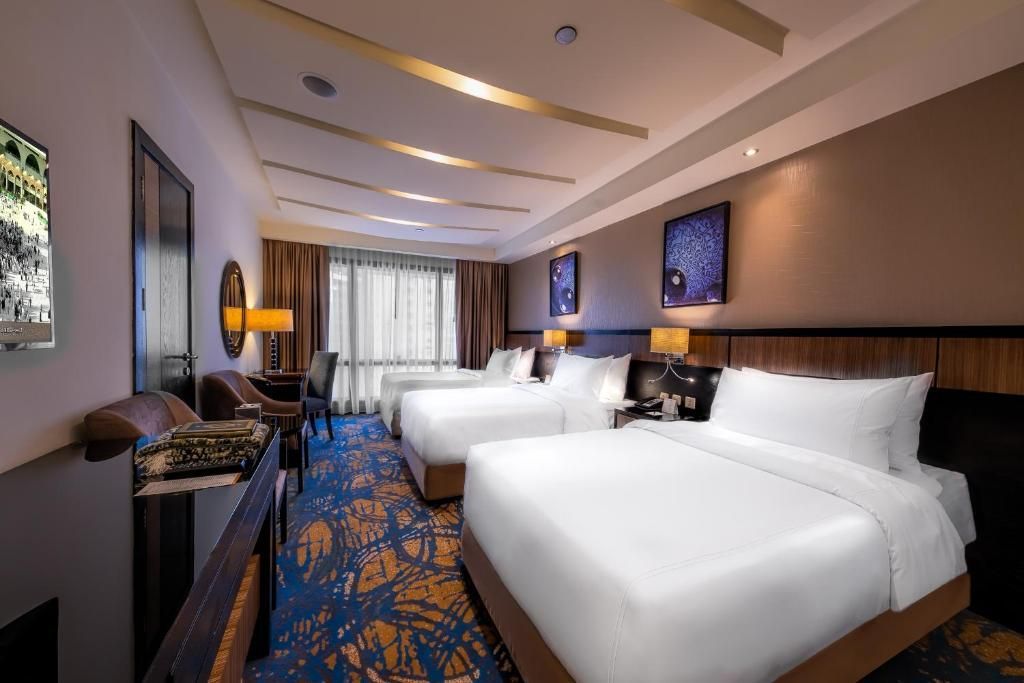Hotel room with three queen beds, art, desk, and patterned blue and gold carpet.