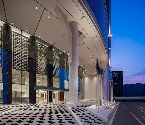 Modern building entrance with columns, glass facade, and checkered floor. Dusk setting.