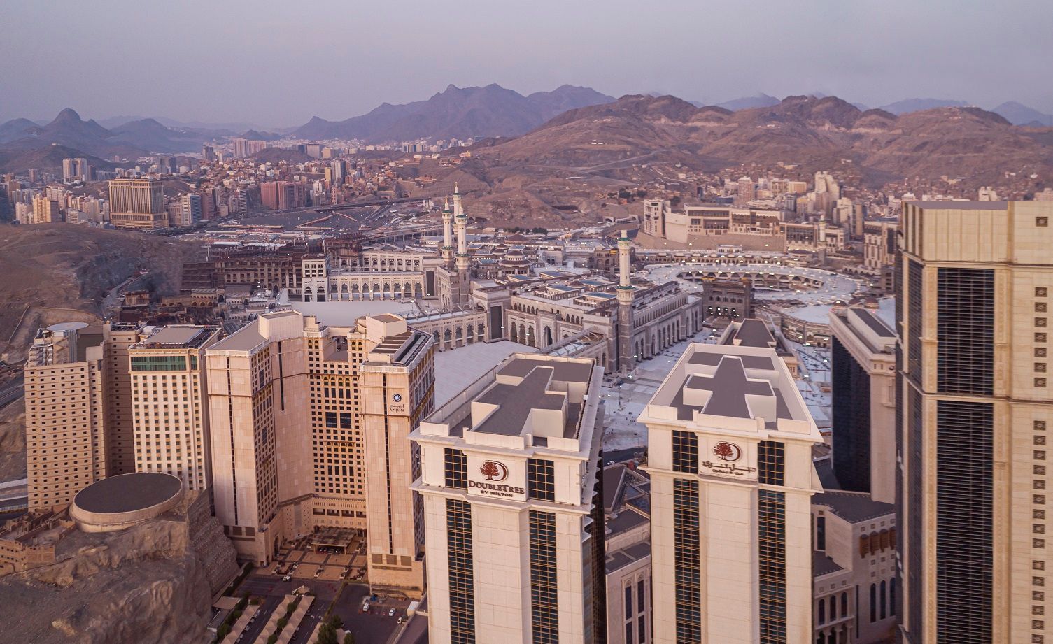 Aerial view of Mecca, Saudi Arabia, with tall buildings and the Grand Mosque visible.