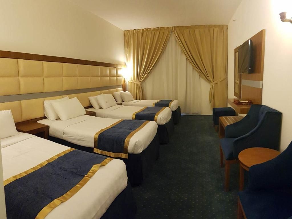 Hotel room with four beds, blue and gold bedding, two armchairs, and a small TV.