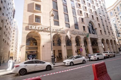 Emaarta Taiba Hotel in Medina, Saudi Arabia, with parked cars and people on the street.