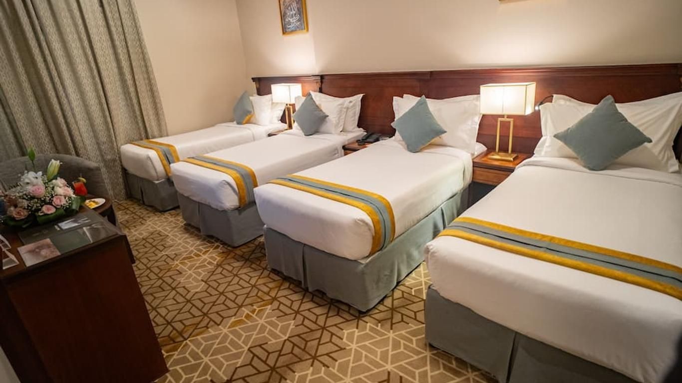 A hotel room with four single beds. White bedding, teal pillows, and bedside lamps.