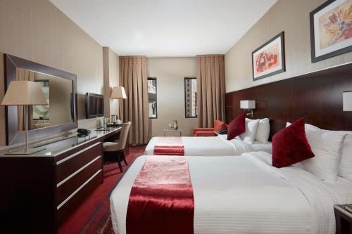 Hotel room with two beds, desk, and large mirror. Red accents.