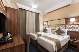 Hotel room with two twin beds, desk, and TV. Neutral colors: brown, beige, white.