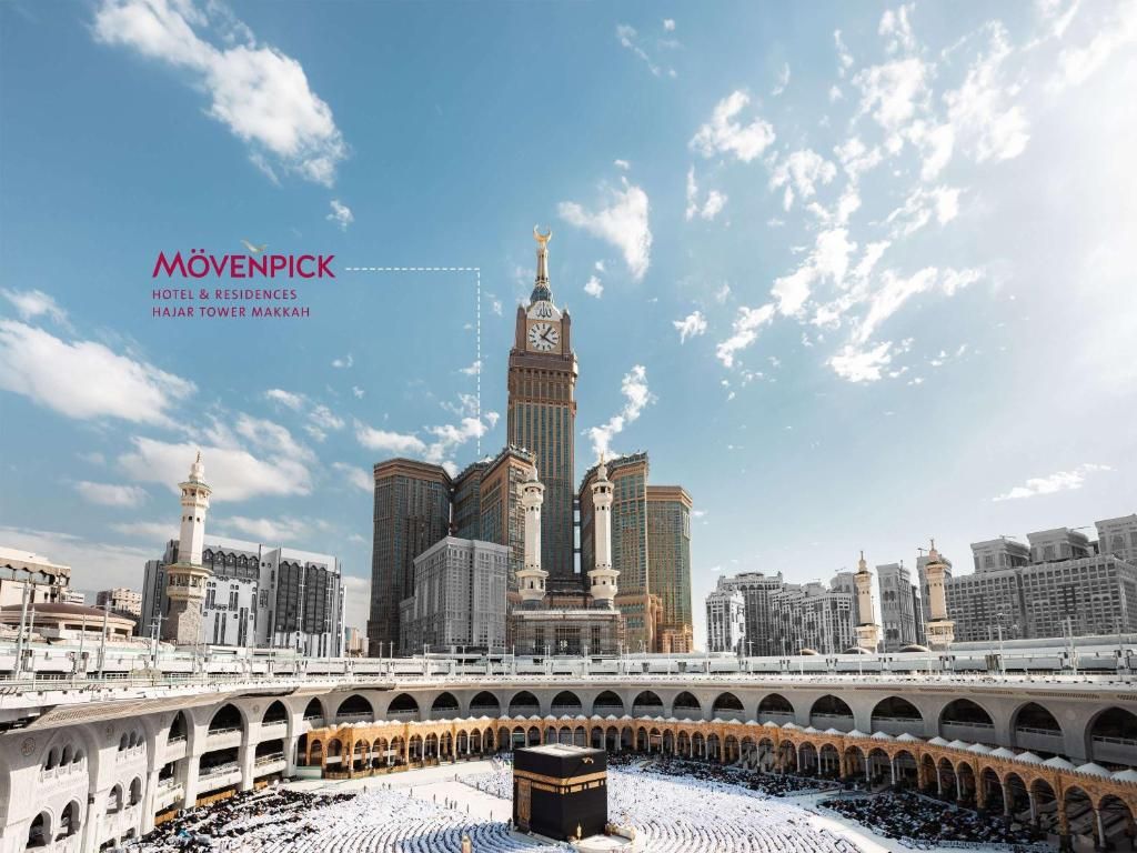 Kaaba and clock tower in Mecca, Saudi Arabia; people circumambulating. Sunny sky.