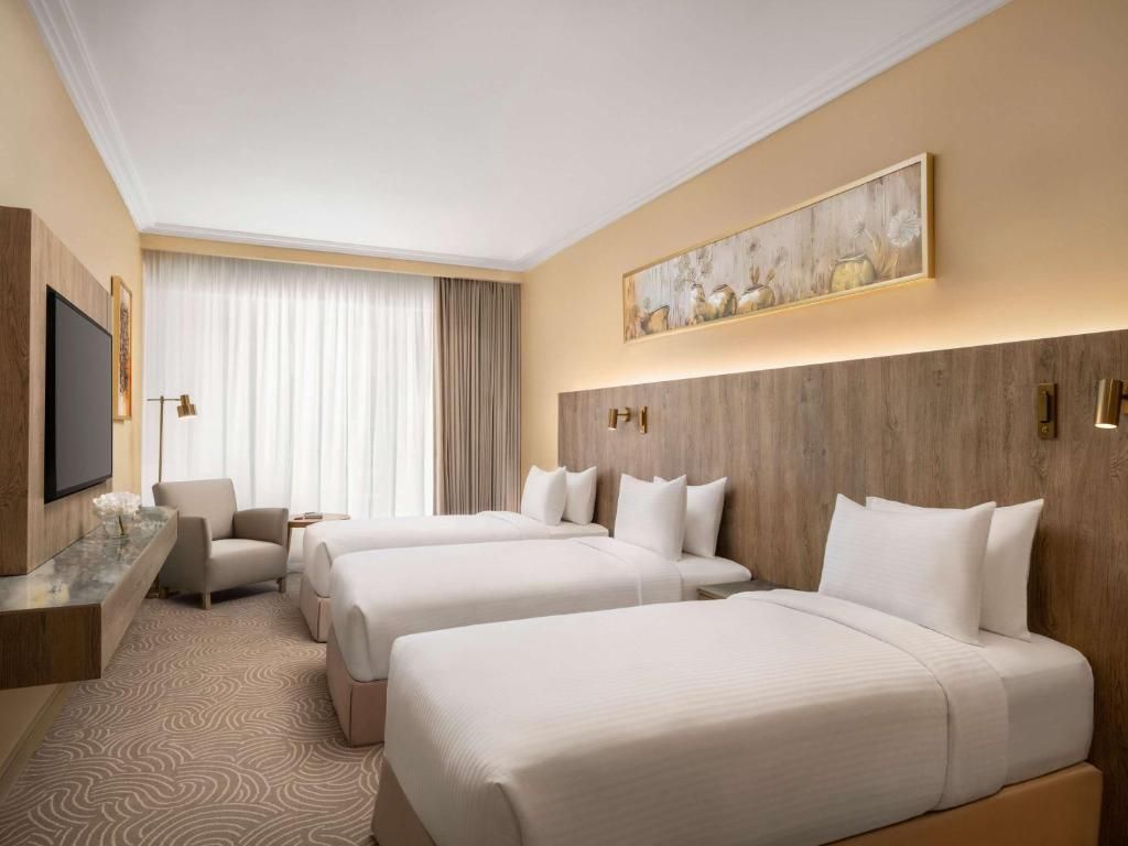 Hotel room with three beds, a TV, chair, and window with curtains.
