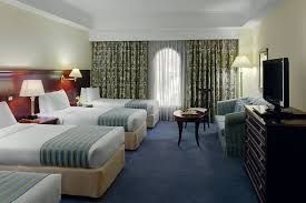 Hotel room with three beds, blue carpet, green patterned curtains, and a TV.