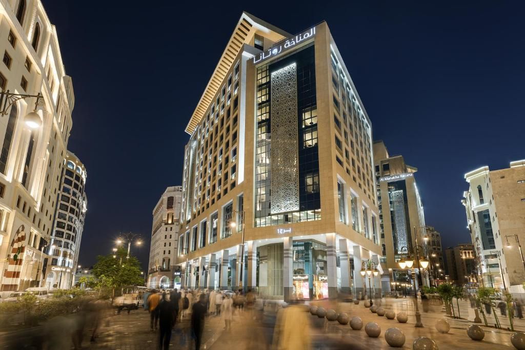 Night view of a modern hotel building in a city. Beige exterior, glass windows, street lights.