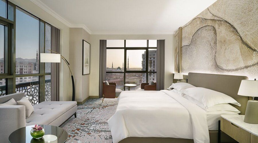 Hotel bedroom with large bed, cityscape view, neutral tones.