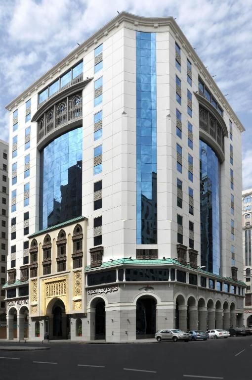 Modern white building with blue glass facade, street view, cars parked nearby.