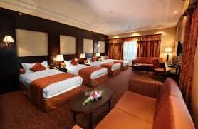 Hotel room with multiple beds, sofas, and a round table. Orange, brown, and white color scheme.