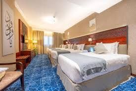Hotel room with multiple beds, blue carpet, and wall decor.