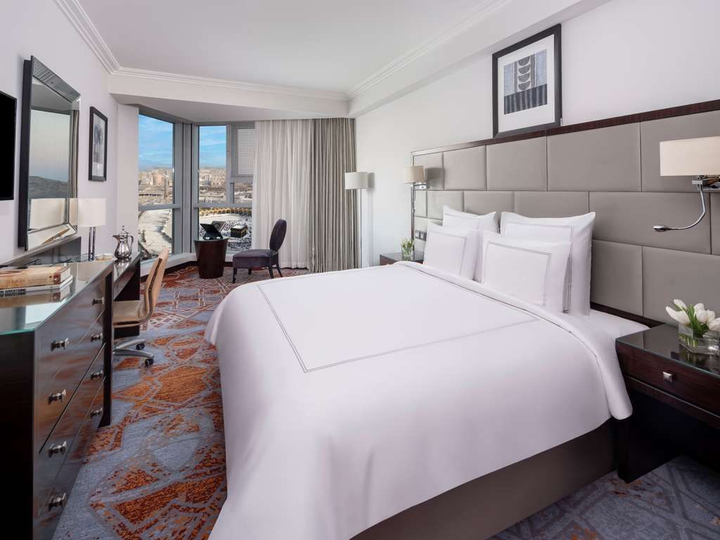 Hotel room with a large bed, desk, and city view from a window.