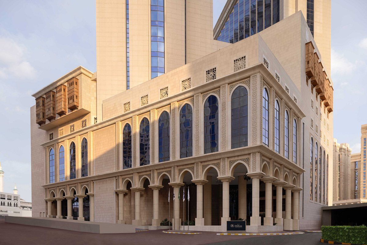 Beige building with arched windows and pillars, part of a tall modern skyscraper, possibly a hotel.