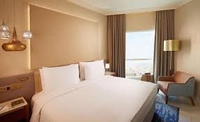 A luxurious hotel bedroom with a large bed, window, and a sitting area.