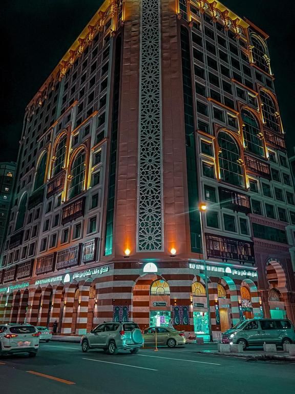 Tall building with ornate design, lit at night. Cars on street below.