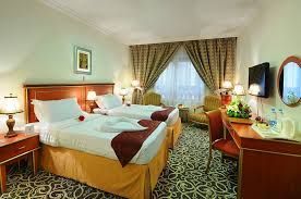 Hotel room with two twin beds, desk, and small TV. Beige, gold, and brown color scheme.