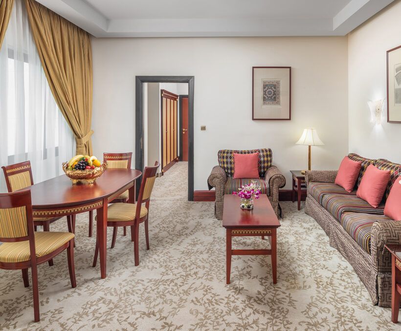 Living room with dining area; brown furniture, beige carpet, and fruit bowl on the table.
