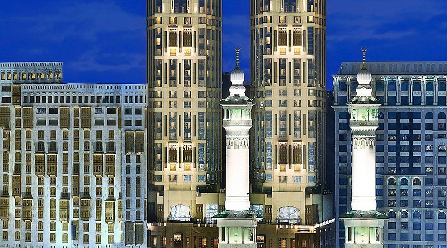 Skyscrapers at night with lit minarets in front, possibly Mecca, Saudi Arabia.
