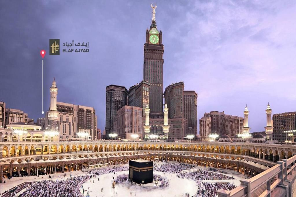 Kaaba at Mecca, surrounded by people, viewed from above. The clock tower is visible in the background.