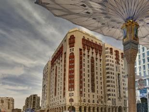 Hotel in Medina, Saudi Arabia, under an umbrella. Beige and brown building with a cloudy sky.