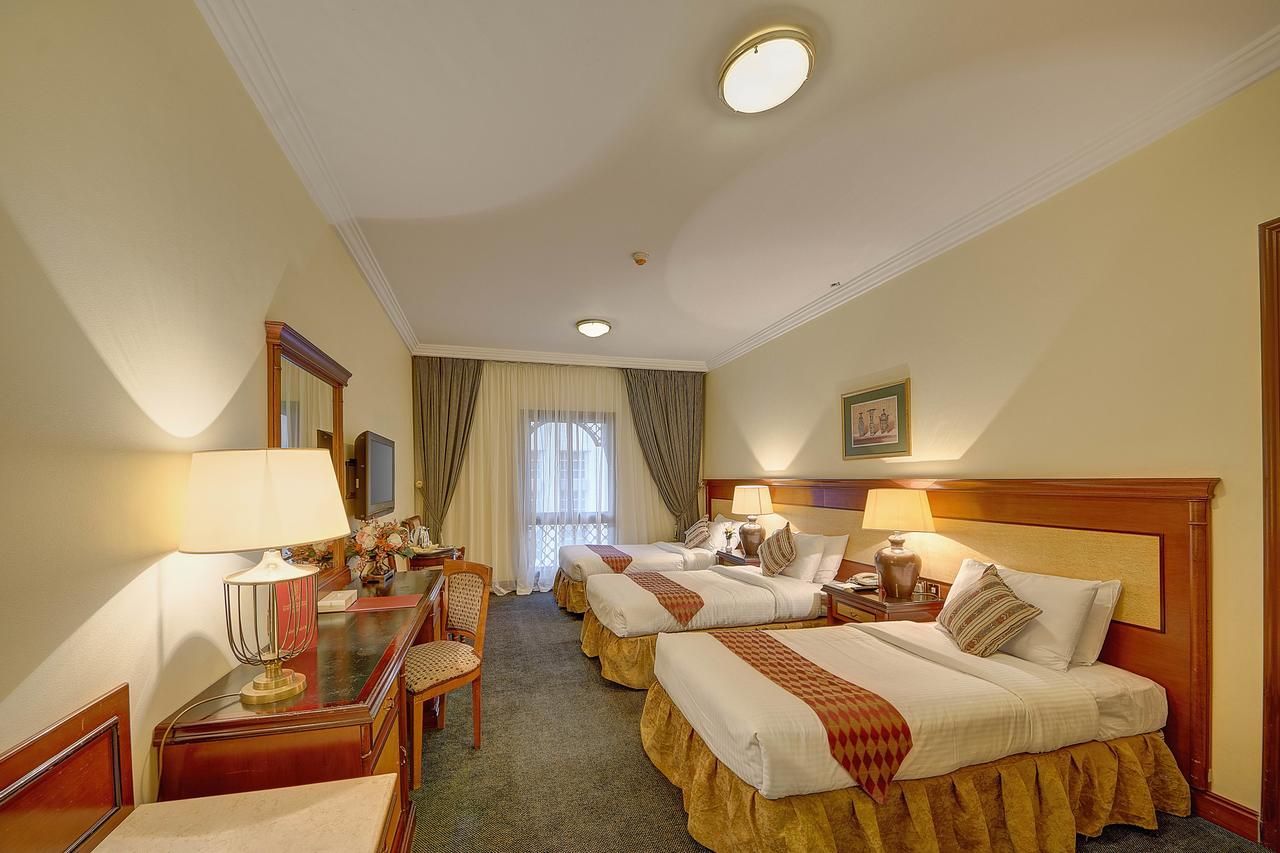 Hotel room with three beds, desk, and curtains.