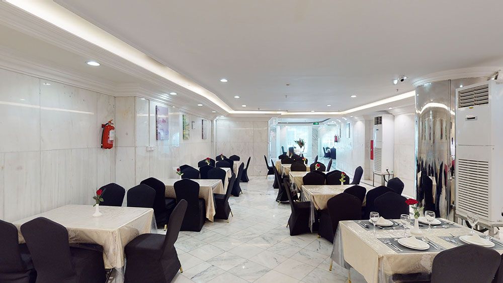 Restaurant interior: tables set with white tablecloths, black chairs, white walls, recessed lighting.