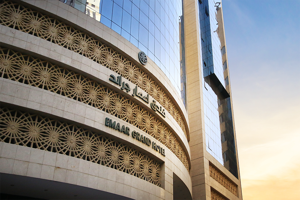 Exterior of Emaar Grand Hotel, featuring ornate stonework and a modern glass facade against a blue sky.