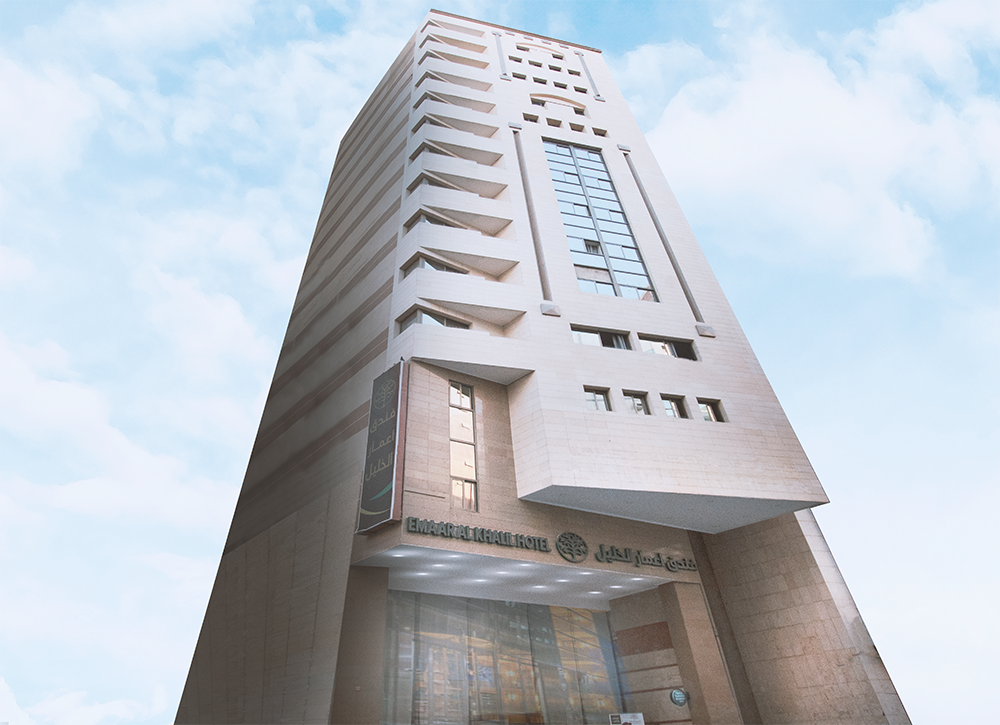 Tall beige high-rise building with a cloudy sky background. Entrance visible, sign in Arabic and English.