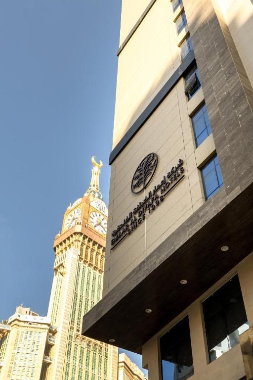 Tall hotel building with sign, clock tower in the background under a blue sky.