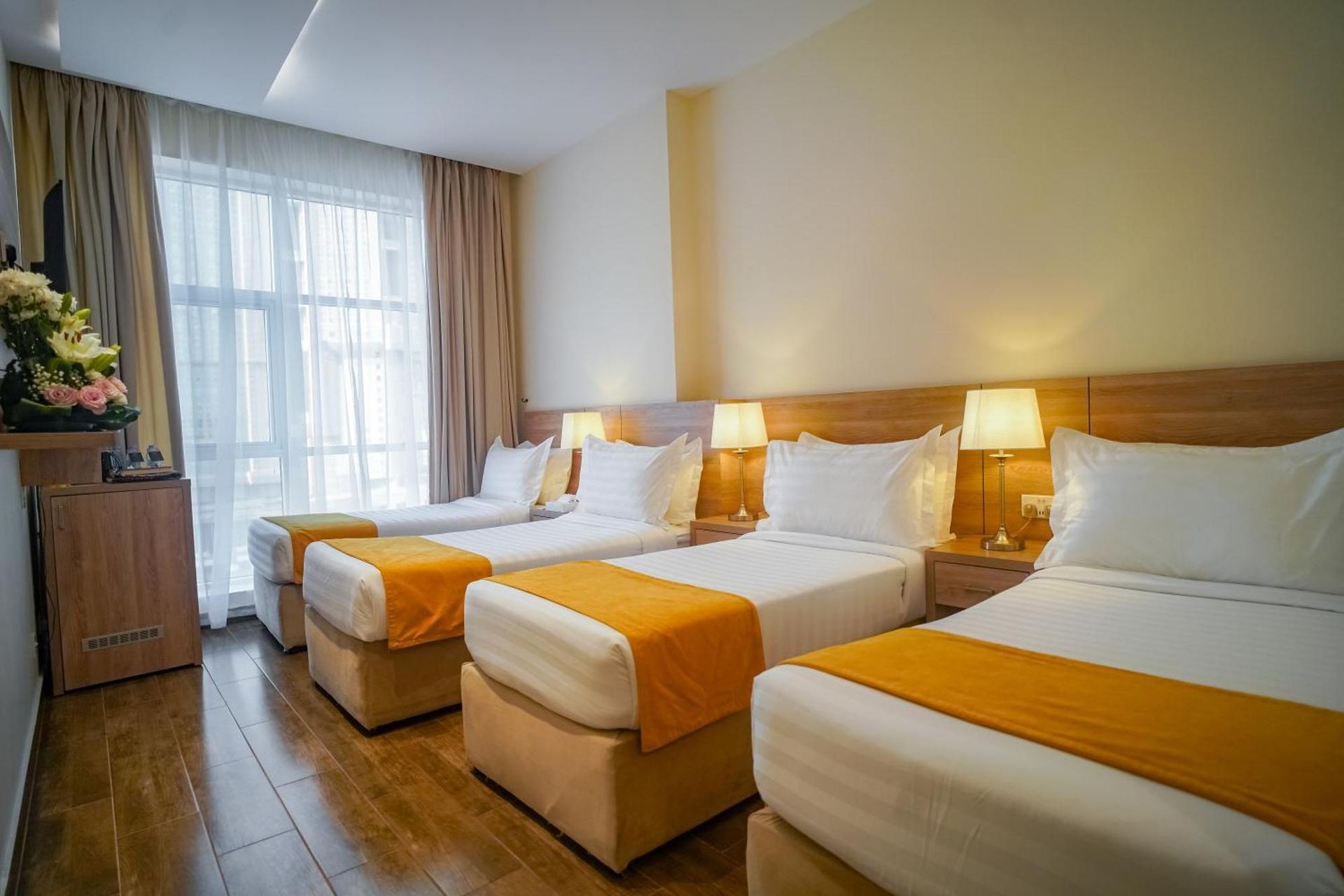 A hotel room with three twin beds, white linens, mustard accents, and bedside lamps.