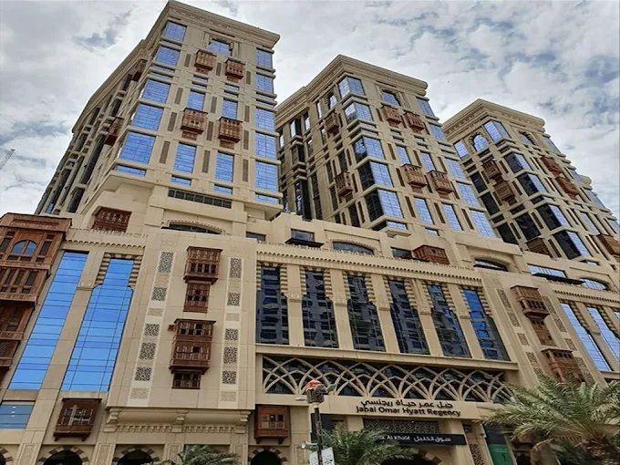 Three beige high-rise buildings with blue windows and wooden balconies, in a Middle Eastern city.
