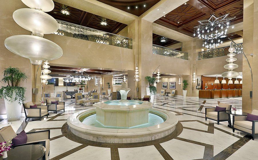 Luxurious hotel lobby with fountain, seating, and ornate lighting.