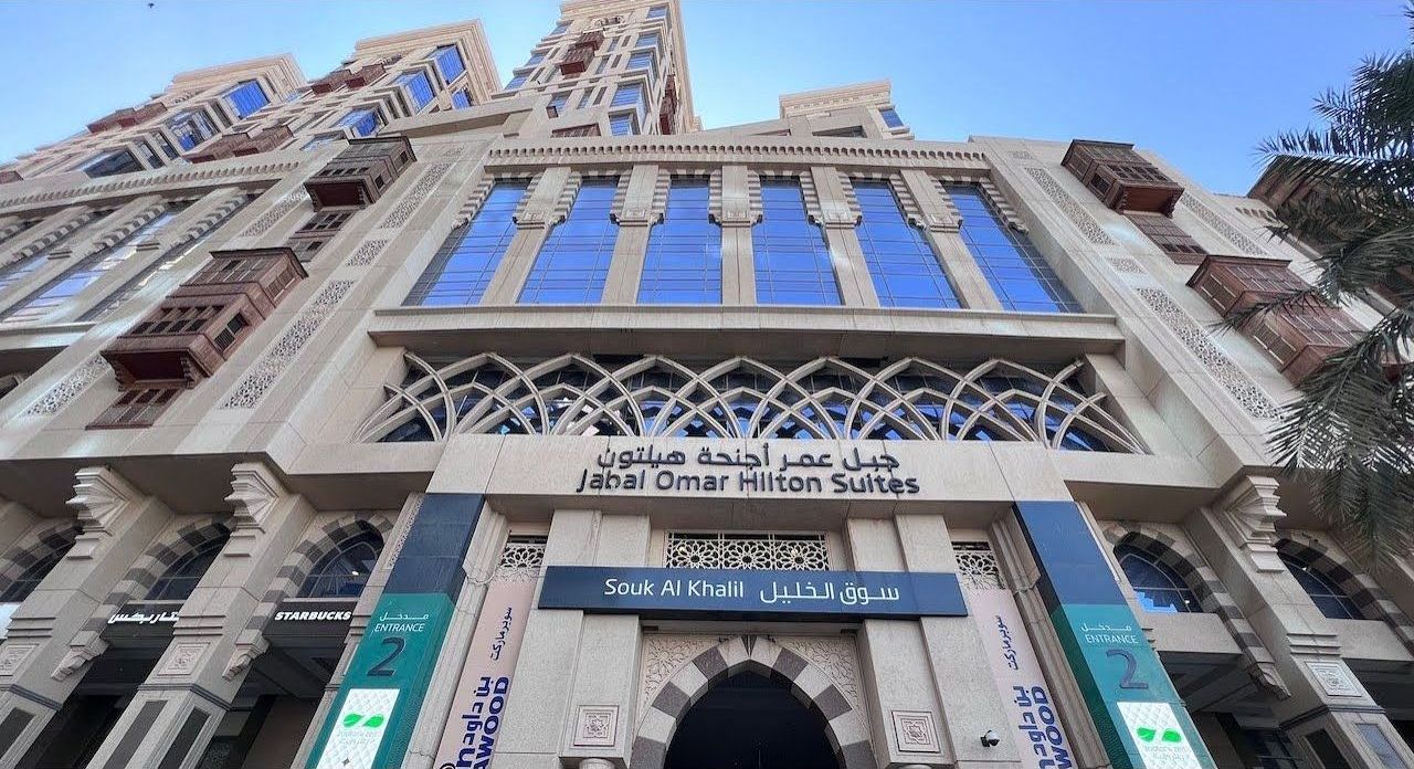 Faisaliah Omar Alfayhan Suites building in Mecca, beige facade with blue windows, arched entryway, sunny day.
