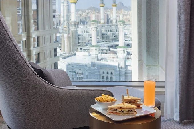 A room overlooking a mosque with a chair, food, and drink on a table.