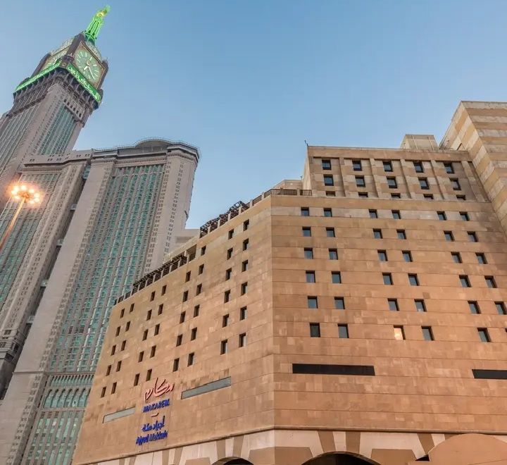 The Abraj Al-Bait Clock Tower and hotel buildings in Mecca, Saudi Arabia, against a blue sky.