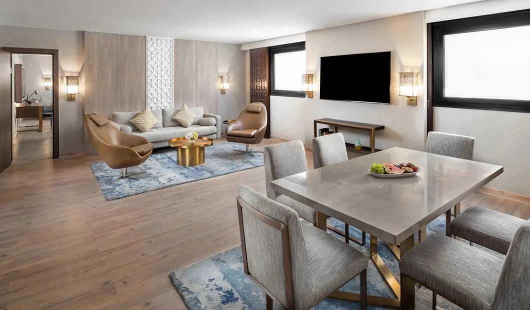 Luxurious hotel suite: living area with sofa, chairs, coffee table, dining table, TV, and open doorway to bathroom.