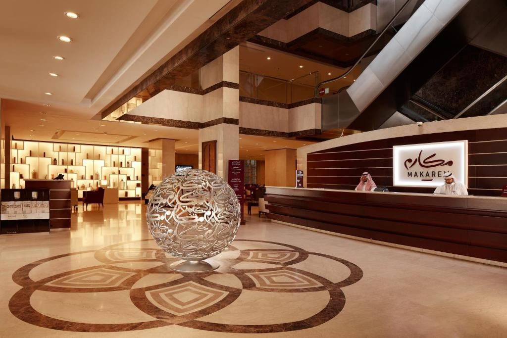 Hotel lobby with a large, ornate sphere sculpture, front desk, and tiled floor with geometric design.