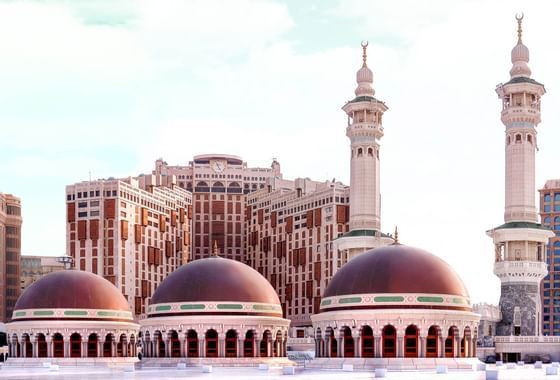 Mosque with red-domed rooftops, tall minarets, and a high-rise building in the background.