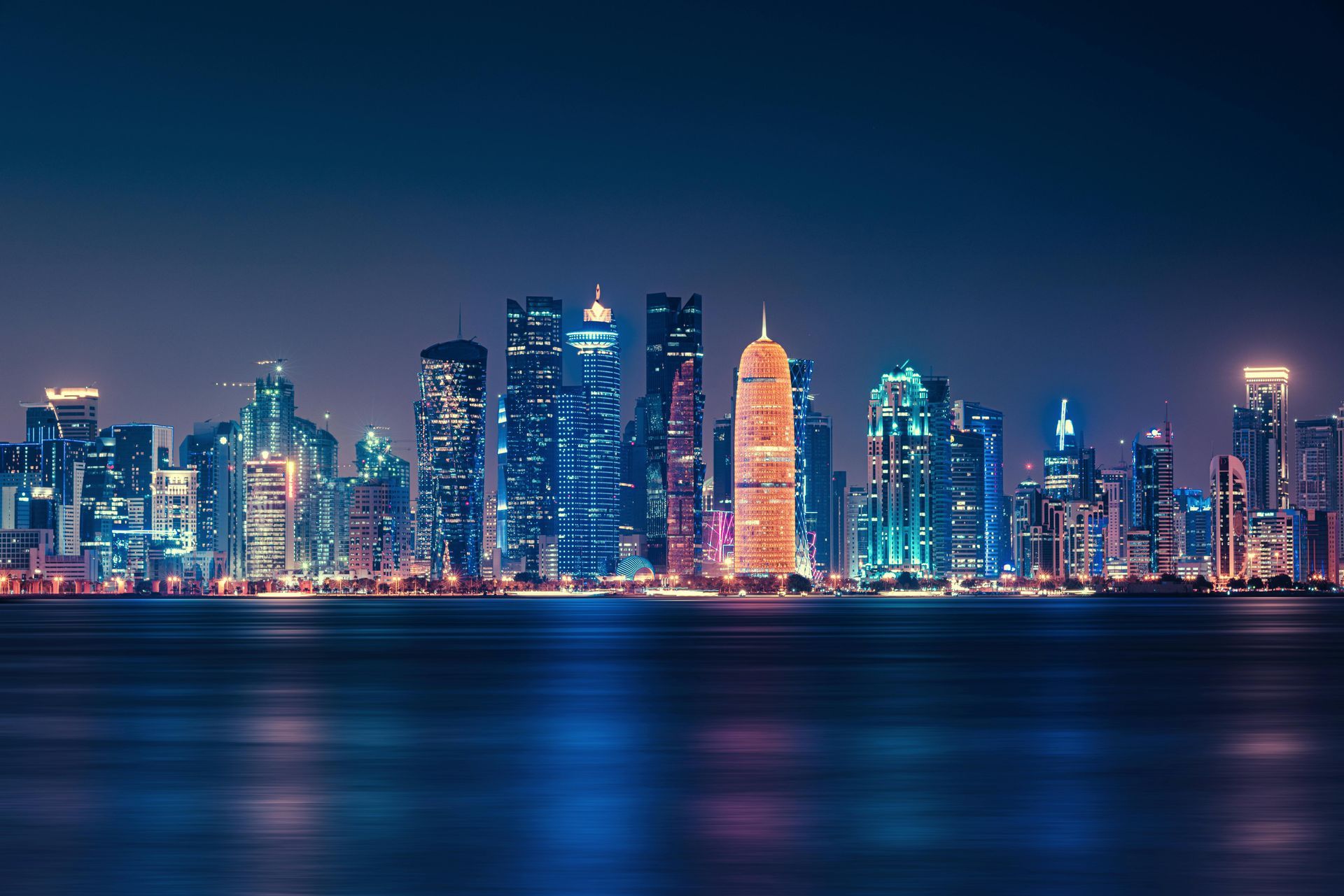 A city skyline at night with a body of water in the foreground.