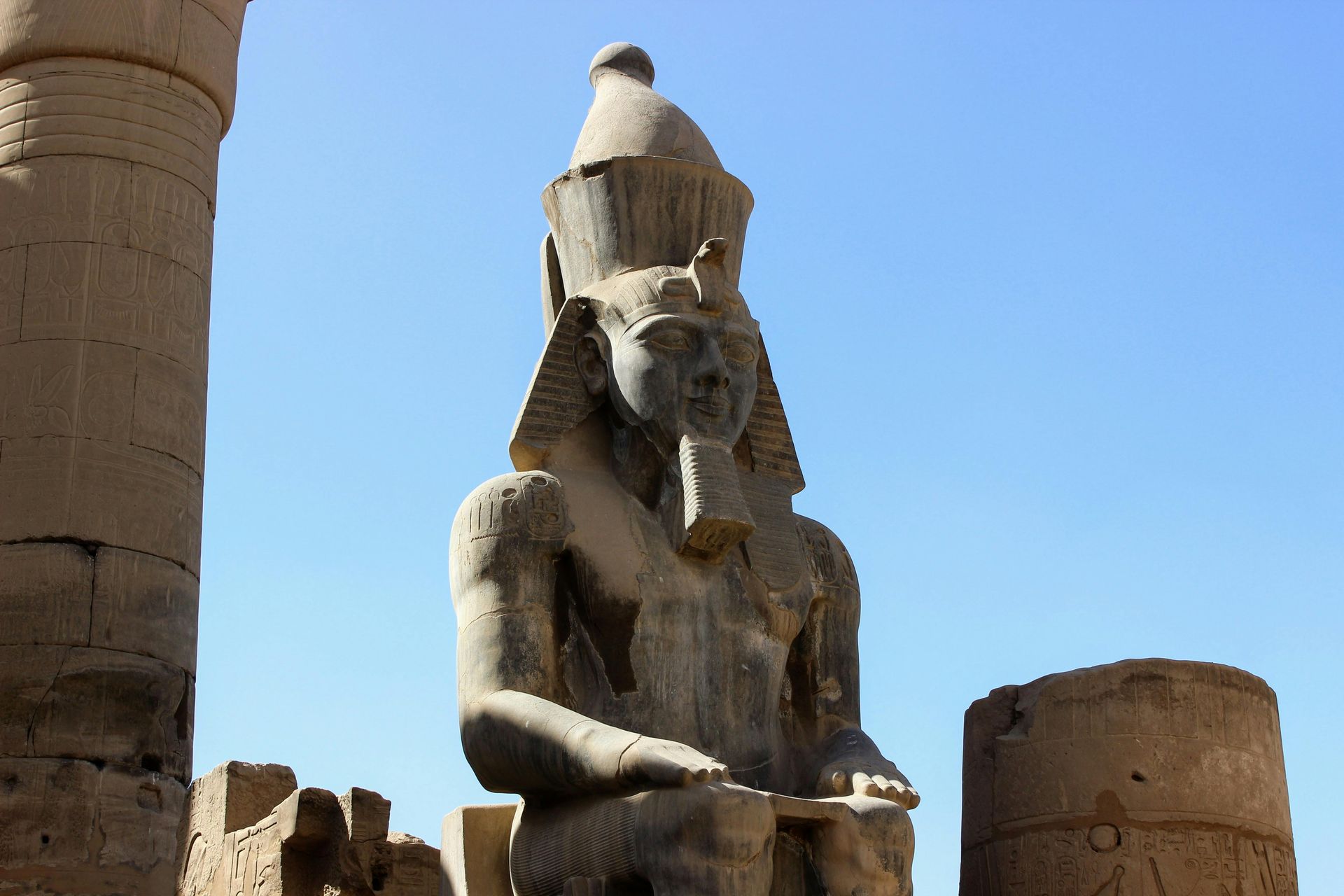 Statue of pharaoh in ornate headdress, seated, stone, in ancient Egyptian temple.