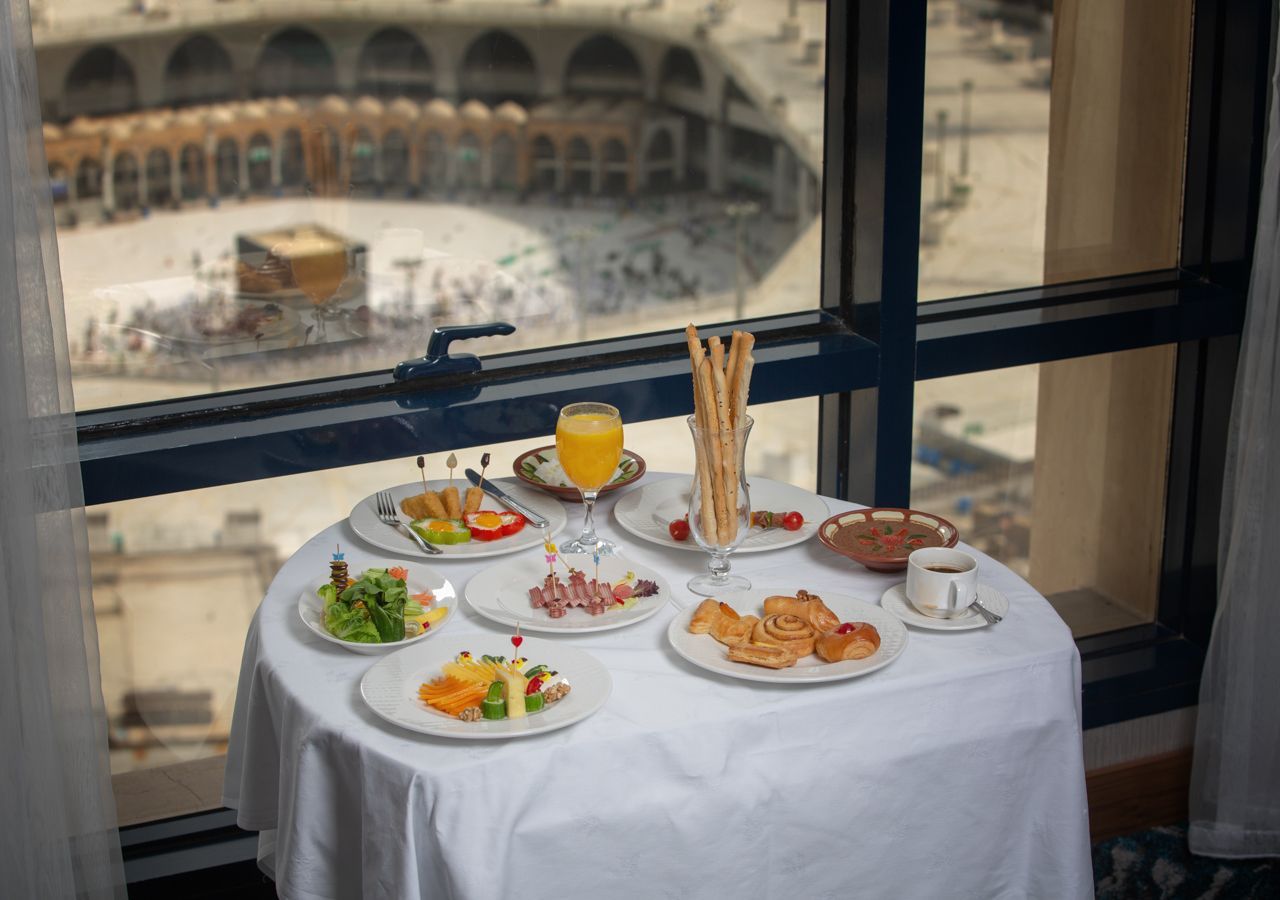 Table set with food, juice, and breadsticks, overlooking the Kaaba in Mecca, Saudi Arabia.