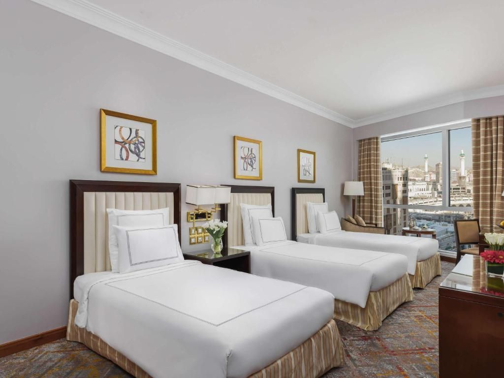 A hotel room with three single beds, gray walls, and a city view.