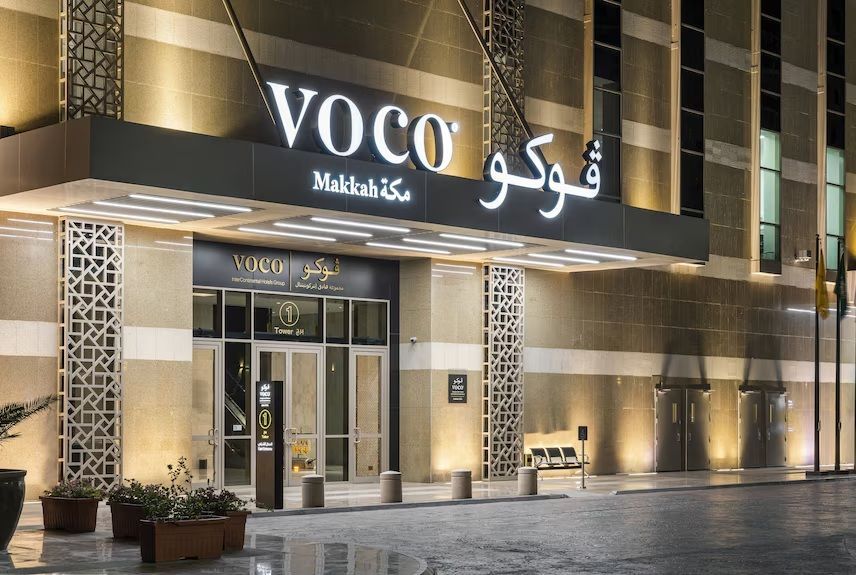 VOCO hotel entrance at night; lit sign and facade with Arabic text.