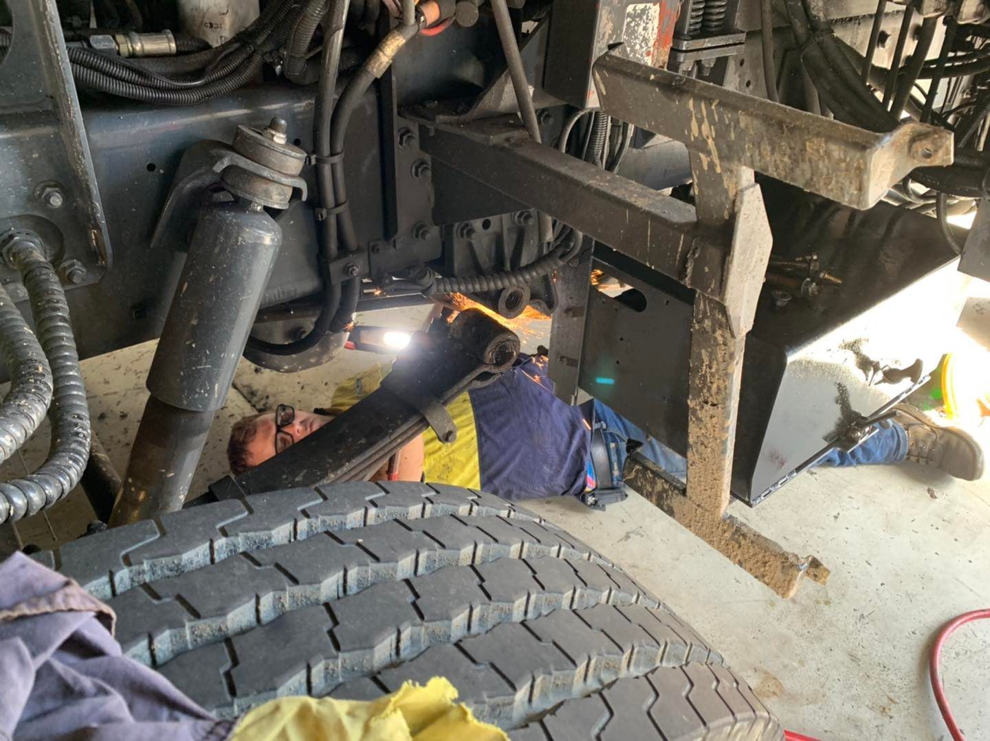Mechanic Working Under a Truck Near a Tire, Using a Light; Indoor Setting — A.M.D. Automotive Services in Mackay, QLD