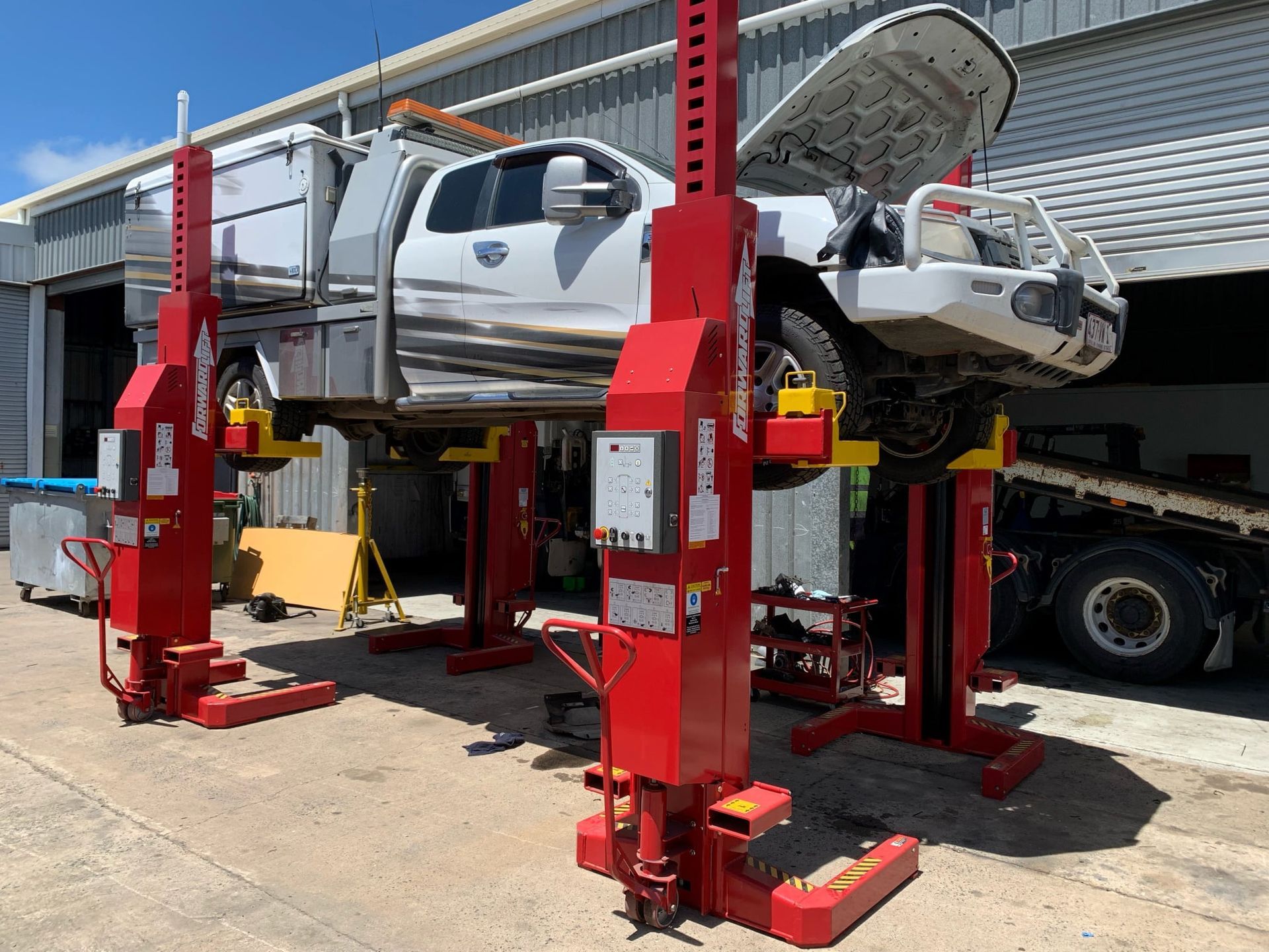White Pickup Truck Raised on Four Red Hydraulic Vehicle Lifts in a Garage — A.M.D. Automotive Services in Mackay, QLD
