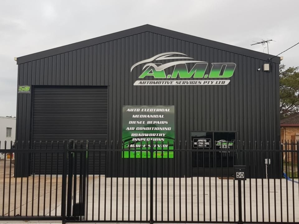 A dark metal warehouse building with green A.M.D. Automotive Services signage and an auto repair service list on the front — A.M.D. Automotive Services in Mackay, QLD
