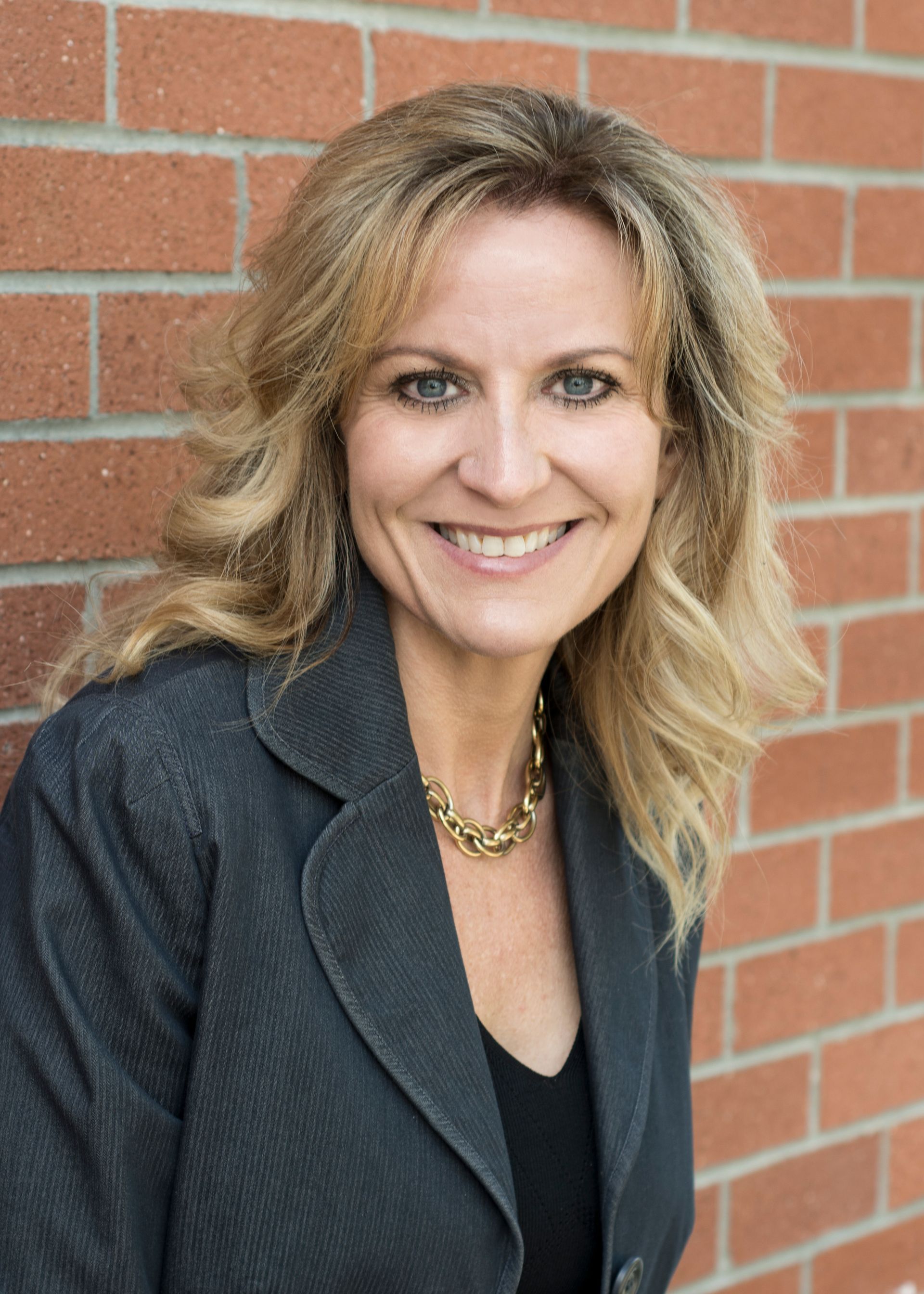 A woman in a suit is smiling in front of a brick wall.