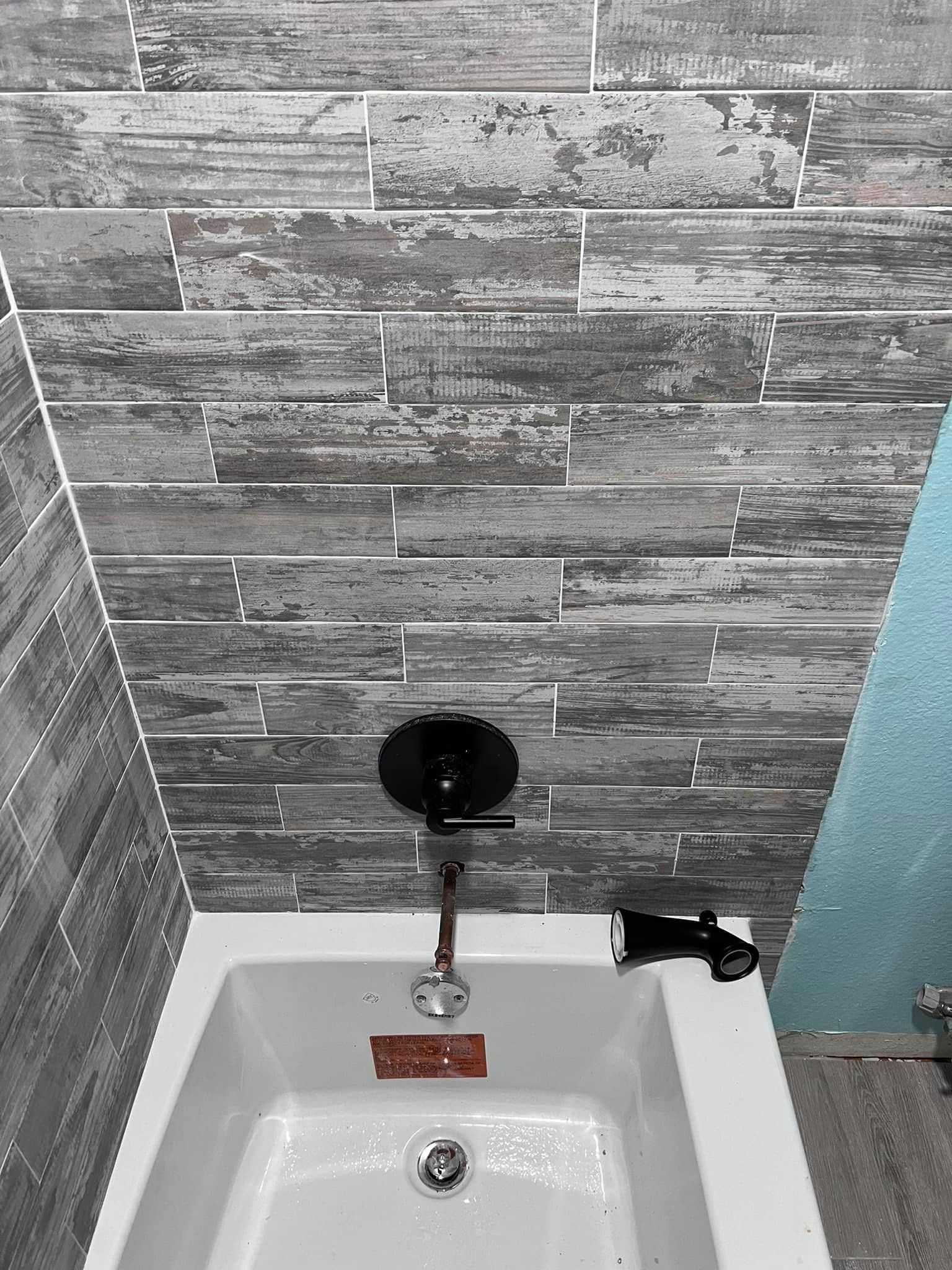 Small bathroom sink with wall-mounted faucet, round black mirror, and gray tile backsplash.